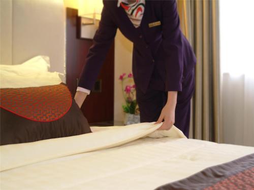 a woman in a hotel room making a bed at Guangdong Hotel-Free Shuttle & Registration Counter Service during Canton Fair in Guangzhou