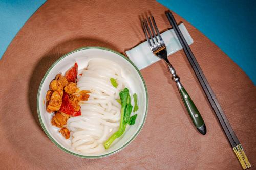 Narat新疆华美胜地那拉提英迪格酒店的桌上放着一碗面条和蔬菜，旁边还有一把叉子。