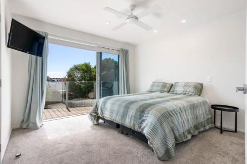 a white bedroom with a bed and a large window at Peaceful Paradise - Waihi Beach Holiday Home in Waihi Beach