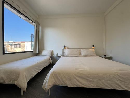 twee bedden in een witte kamer met een raam bij Scandi Haus near ChinaTown in Bangkok