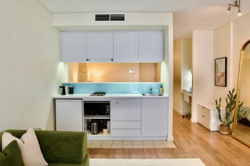 a kitchen with white cabinets and a green couch at Modern Barangaroo Apartment with Waterfront Balcony Views & Private Parking in Sydney