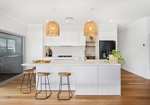 a kitchen with white cabinets and bar stools at Coastal Nest - Walk to Windang Beach in Windang