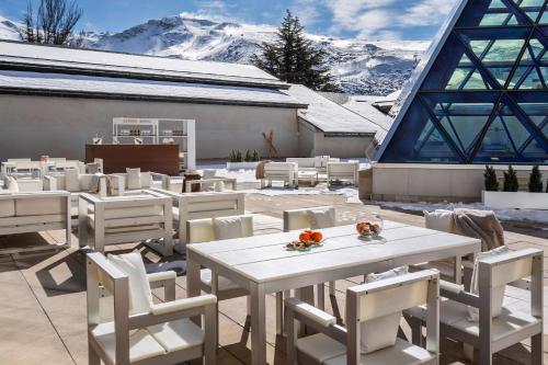 a patio with white tables and chairs and snow covered mountains at Meliá Sol y Nieve in Sierra Nevada