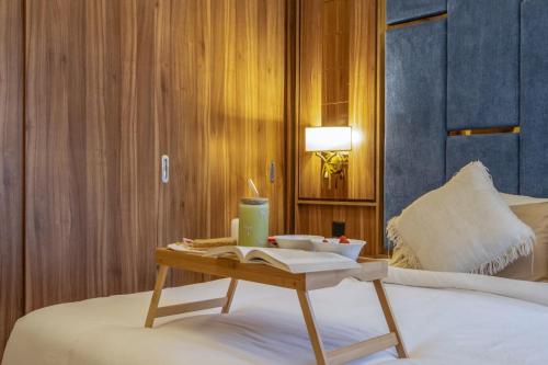 a bed with a table with a book on it at Emora 1 BR Apartment in Dubai