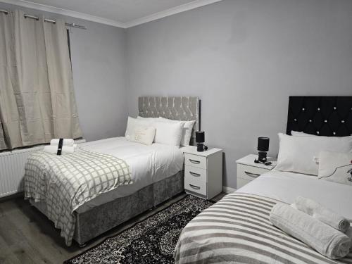 two beds in a bedroom with white walls at Heathrow roomzzzz BnB in Hayes