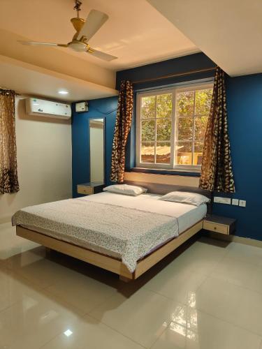 a bedroom with a bed with a blue wall and a window at Guesthouse Sakina Colva in Colva