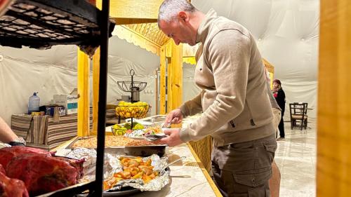 Ein Mann, der Essen auf einem Tisch mit Fleisch zubereitet. in der Unterkunft HAGIA SOPHIA lUXURY CAMP in Disah