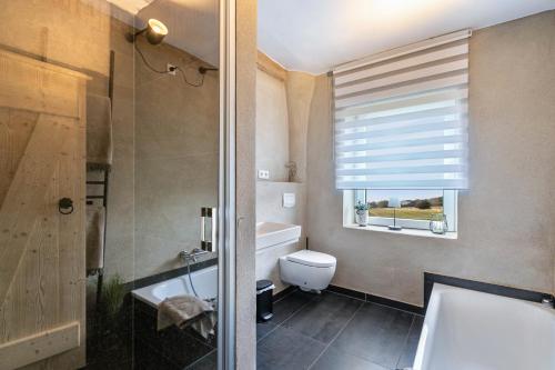 ein Badezimmer mit Badewanne und Toilette und einem Fenster in der Unterkunft Lehmhuus in Klanxbüll