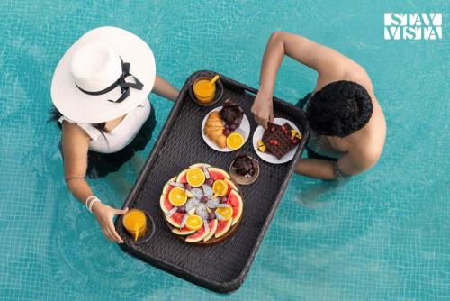 two people in a swimming pool with a tray of food at StayVista at Acasa with Lawn in Alibaug