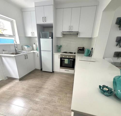 Blue Beach Haven في Cape Town: مطبخ مع أجهزة بيضاء ودواليب بيضاء