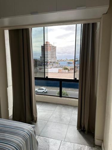 een slaapkamer met een groot raam met uitzicht op de stad bij Hyago Monteiro in Capão da Canoa