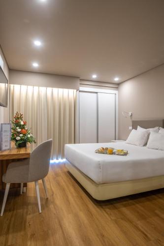 a bedroom with a large white bed and a desk at Hotel Cristal Caldas in Caldas da Rainha