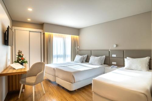 a hotel room with two beds and a desk at Hotel Cristal Caldas in Caldas da Rainha