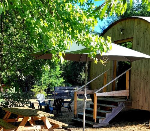 " village tonneaux de tirpoil " في Montilliers: طاولة نزهة ومظلة بجانب طاولة وكراسي
