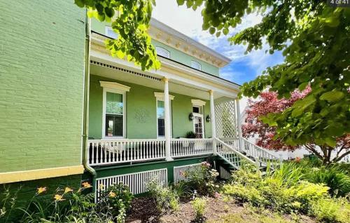 a green house with white railings and a porch at Wisteria Suite -The Belvedere Inn in Oswego