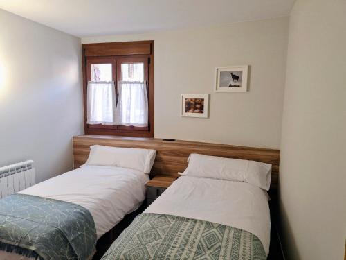 zwei Betten in einem kleinen Zimmer mit Fenster in der Unterkunft Apartamentos Casa Domec in Castejón de Sos