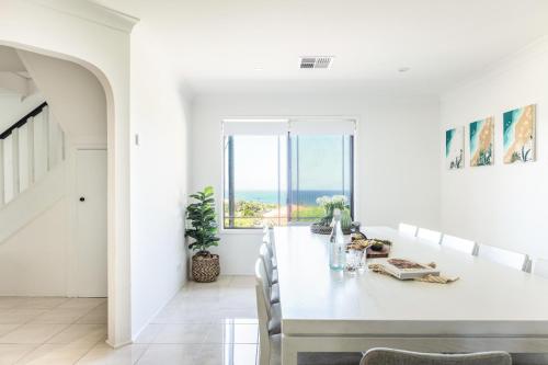 a white dining room with a table and a view of the ocean at Oceans 21 Caves Beach in Caves Beach