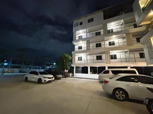 Dos coches estacionados en un estacionamiento frente a un edificio. en Comfy Hotels Share Bathroom คอมฟี่ โฮเทล ห้องน้ำรวม ซอยกิ่งแก้ว 31ก, en Samutprakarn