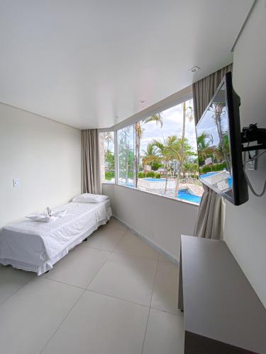 a white room with a bed and a large window at Bosque do Porto Praia Hotel in Porto Seguro