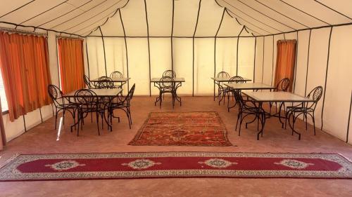 ein leeres Zelt mit Tischen, Stühlen und einem Teppich in der Unterkunft Arawan Luxury Desert Camp at Erg Lihoudi in Mhamid
