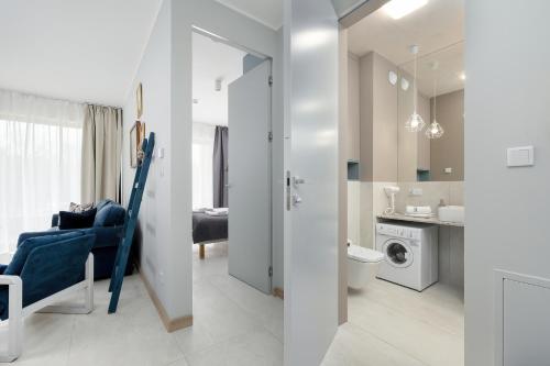 ein weißes Badezimmer mit einem blauen Stuhl und einer Waschmaschine in der Unterkunft GREENERI PARK - Ambria Apartments in Świnoujście