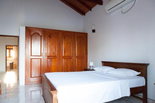 a bedroom with a white bed with a wooden cabinet at Sri Lagoon Villa in Negombo