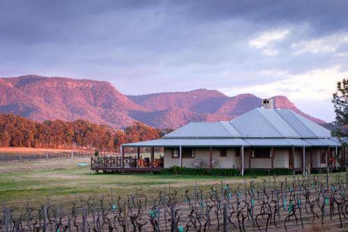 a house in a vineyard with mountains in the background at Hanging Tree Wines in Pokolbin