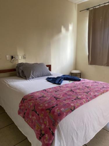 a bed with a pink blanket on top of it at Quarto econômico no centro in Sete Lagoas