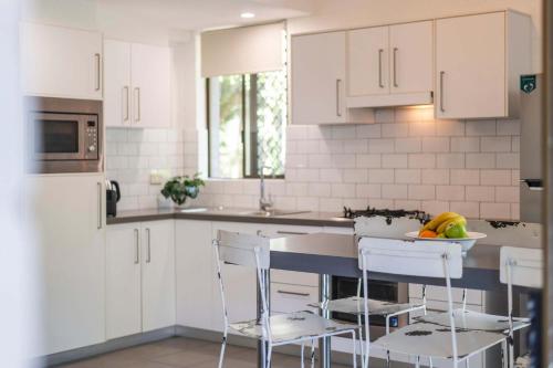 Bayshore Bungalow 14 - Oceanstays في خليج بايرون: مطبخ مع دواليب بيضاء وكاونتر مع الكراسي