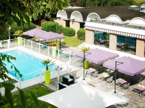 an overhead view of a pool with tables and purple umbrellas at Hôtel Novotel Valenciennes in Valenciennes