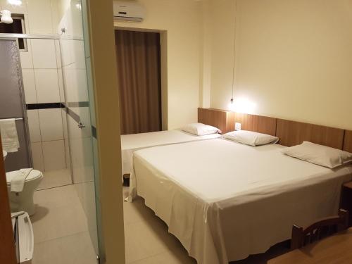 two beds in a hotel room with a bathroom at Oft Place Hotel in Goiânia