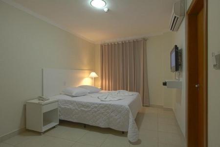 a white bedroom with a bed and a night stand at Skala Traveling Hotel in Cuiabá