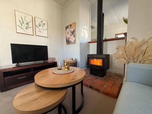Hawke's Bay Escape - Railway Cottage في هاستينغز: غرفة معيشة مع طاولة وموقد خشبي