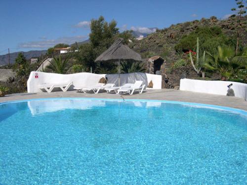 una gran piscina azul con 2 sillas blancas en La Hacienda BuenVivir - Apartamentos, en Los Llanos de Aridane