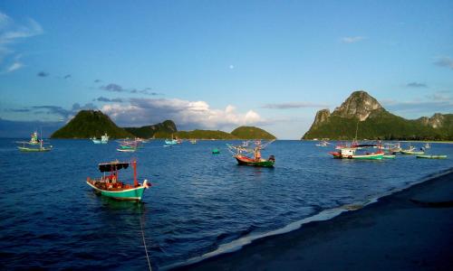a group of boats in the water with mountains in the background at SeeSea Thai wooden house on beachfront in Prachuap Khiri Khan