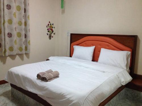 a bed with an orange headboard with a towel on it at Kanda Guesthouse in Si Racha