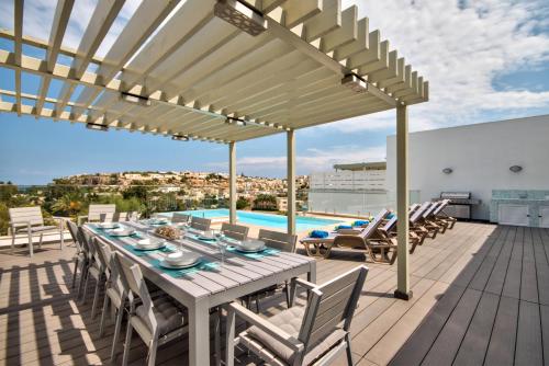 eine Terrasse mit einem Tisch, Stühlen und einem Pool in der Unterkunft Villa Gaia - Sunset Views, Indoor Heated Pool, Sauna and Games Room in Mellieħa