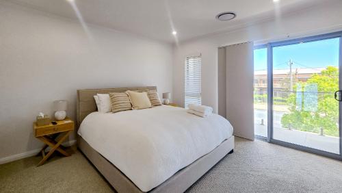 a white bedroom with a bed and a large window at Kincaid Travellers Townhouse - Central Wagga in Wagga Wagga