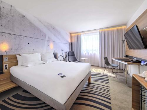 una camera d'albergo con un grande letto bianco e una scrivania di Novotel Kraków Centrum a Cracovia