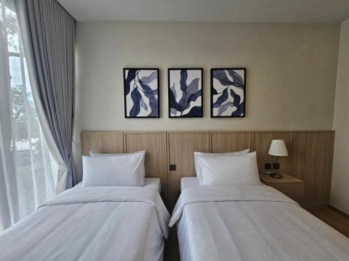 two beds in a room with three paintings on the wall at Wora Phuket in Ban Sam Kong