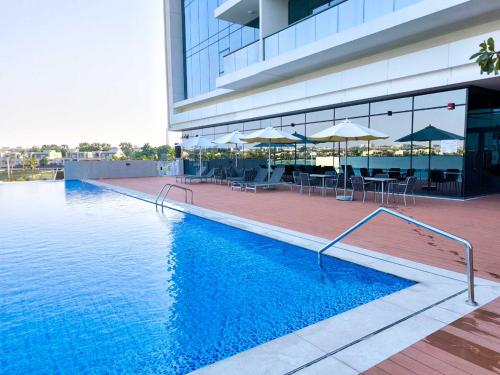 a swimming pool in front of a building with tables and umbrellas at Chic & Bright 1BR Lagoon Suite in Gateway II in Ras al Khaimah