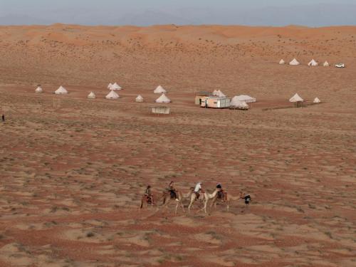 un grupo de personas montando camellos en el desierto en Desert Diamond Private Camp, en Badīyah