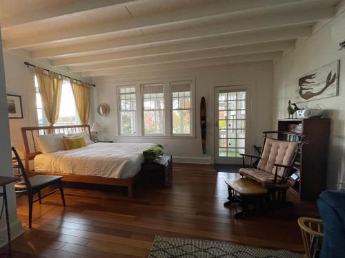 a bedroom with a bed and two chairs and windows at Weems Creek Cottage, Annapolis Waterfront in Annapolis