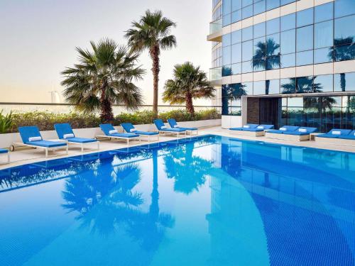 a swimming pool with lounge chairs and a building at Novotel Dubai Al Barsha in Dubai