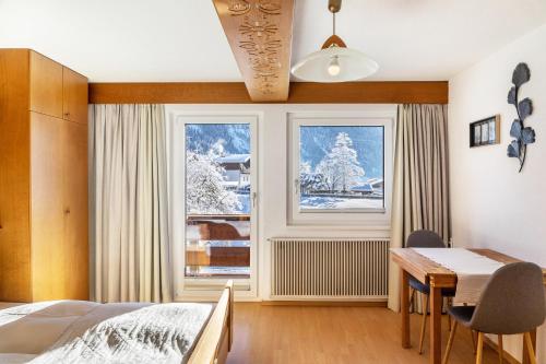 ein Schlafzimmer mit einem Bett und einem Tisch und zwei Fenstern in der Unterkunft Landhaus Perktold in Nesselwängle