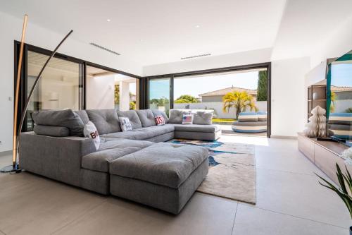 een woonkamer met een grijze bank en glazen deuren bij Villa Boston luxury home with pool and Cali vibes in Le Grau-dʼAgde