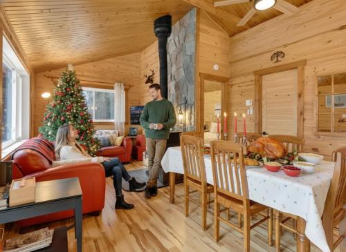 Private beach with SPA on the lake I Plage Sucrée في Saint-Rémi-dʼAmherst: رجل وامرأة يقفان في غرفة المعيشة مع شجرة عيد الميلاد