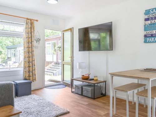 ein Wohnzimmer mit einem Tisch und einem Fernseher an der Wand in der Unterkunft 5 The Glade in Bude