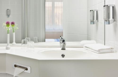 ein weißes Badezimmer mit Waschbecken und Spiegel in der Unterkunft Hotel Magdeburg City Center by Leonardo Hotels in Magdeburg