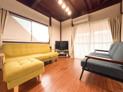 a living room with a yellow couch and a television at まるとくハウス霧島 in Kirishima